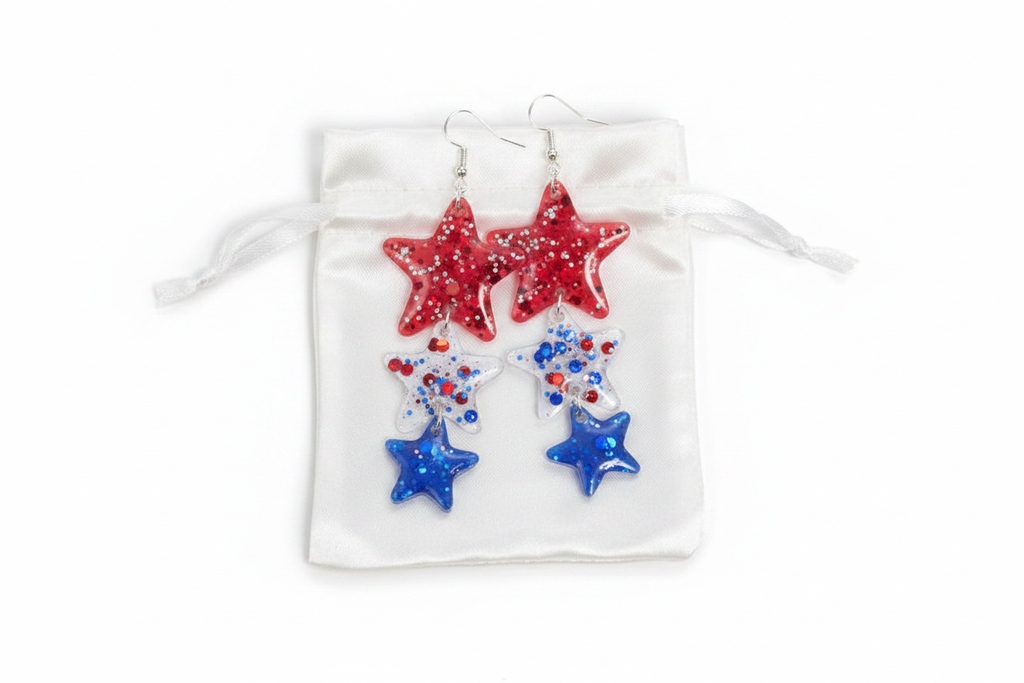 Patriotic red and blue glitter star resin earrings on white satin pouch