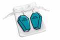 Teal blue coffin-shaped Mad Woman resin earrings on white satin pouch